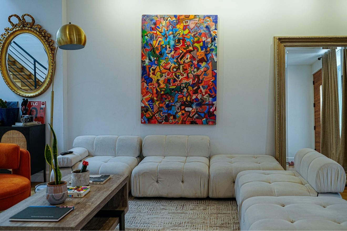 Lounge corner with cream modular sofa, colorful abstract painting, and vintage mirrors